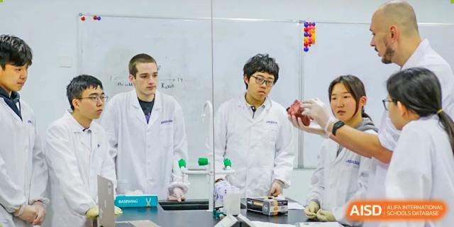 Two students in white lab coats focused on a science experiment with beakers and wires in a lab at the Qingdao Amerasia International School.