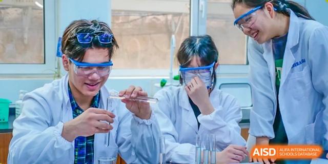 Two students in white lab coats and safety glasses working on a science experiment with a test tube and beaker at the Qingdao Amerasia International School.