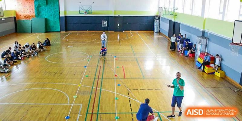 A coach observing a young student on a two-wheeled self-balancing scooter on a basketball court lined with training cones at the Qingdao Amerasia International School.