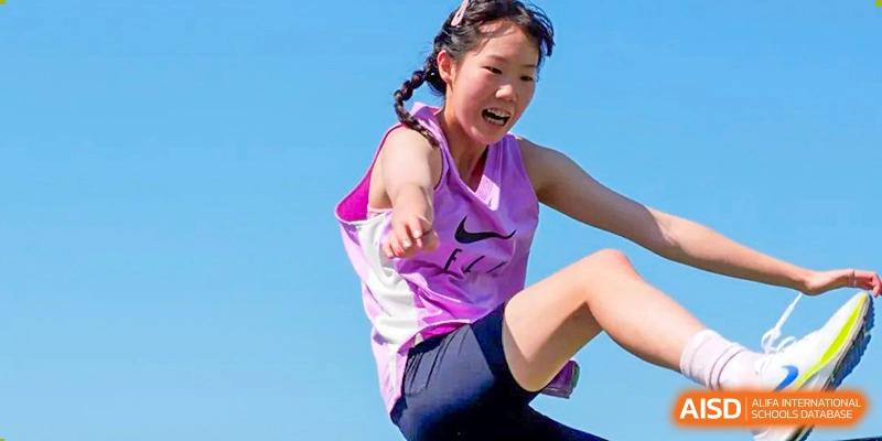 A female student in a purple sports top and black shorts jumping during a track and field event at the Qingdao Amerasia International School.