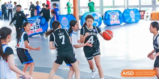 Two teenage players in black and white uniforms guarding a player with the ball during a basketball game at the Qingdao Amerasia International School.