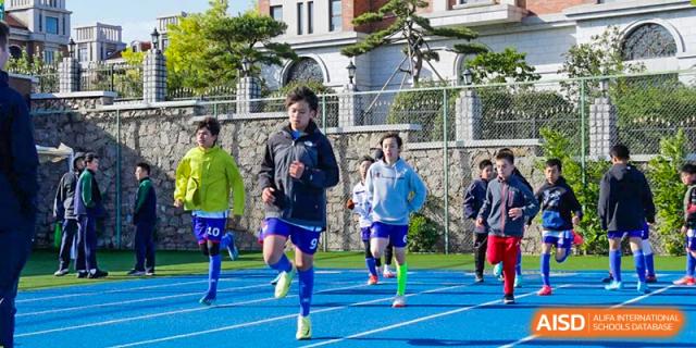 Students in blue uniforms running on a turf field during a sports event at the Qingdao Amerasia International School.