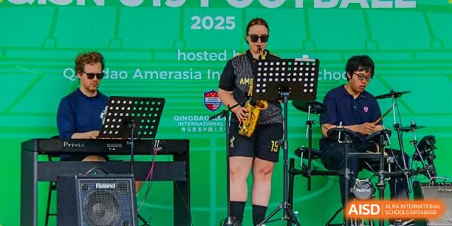 A male musician wearing sunglasses playing a saxophone on a stage at an event hosted by the Qingdao Amerasia International School.