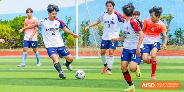 Two male students in soccer uniforms competing for the ball on a turf field during a game at the Qingdao Amerasia International School.