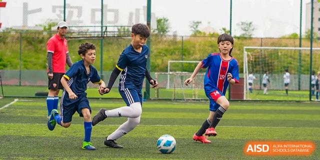 Two male students playing soccer, one dribbling the ball while the other defends, on a turf field at the Qingdao Amerasia International School.