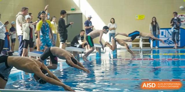A group of students diving into a swimming pool from the edge at the Qingdao Amerasia International School.
