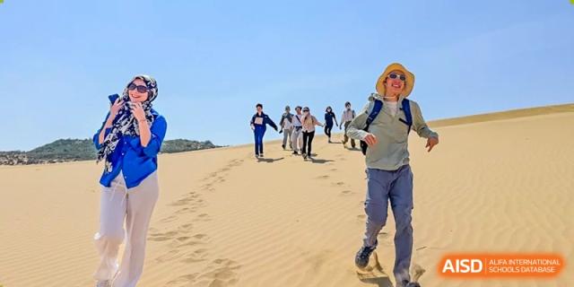 A group of students and teachers walking in a line across sand dunes during a school trip from the Qingdao Amerasia International School.