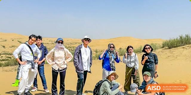 A group of students and teachers posing for a photo in a desert landscape during a school trip from the Qingdao Amerasia International School.
