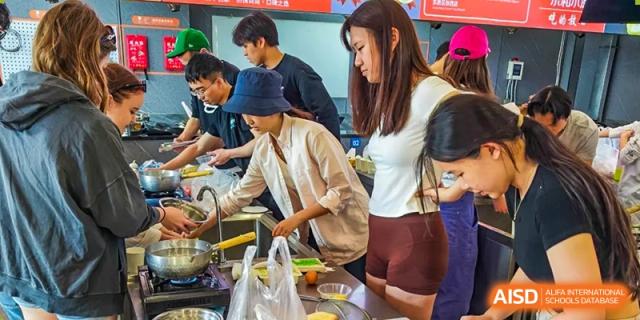 A group of students in a kitchen, with one female student in a bucket hat preparing food at the Qingdao Amerasia International School.