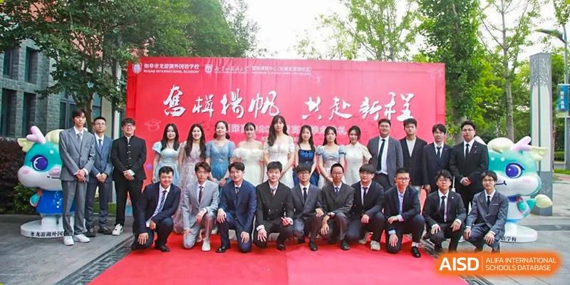 A group photo of students and teachers from Rugao International Academy BFSU on a red backdrop.
