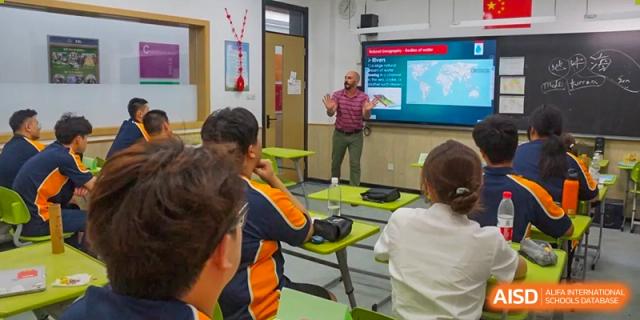 A male teacher gesturing while presenting in front of a smart board to a small group of students at Shanghai Wenlai International School.