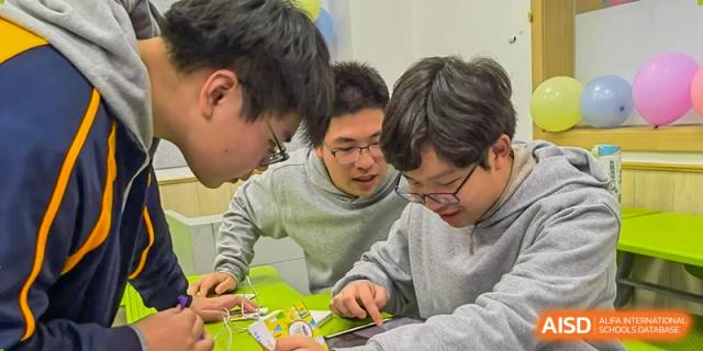 A close-up of three male students working together on a project or assignment, looking intently at a table at Shanghai Wenlai International School.