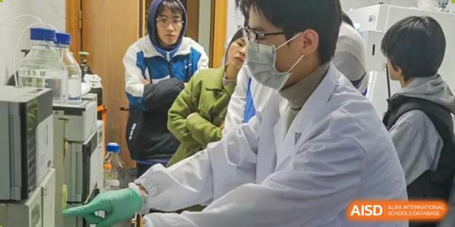 A teacher wearing a lab coat and a face mask looking on as students observe or participate in an experiment at Shanghai Wenlai International School.