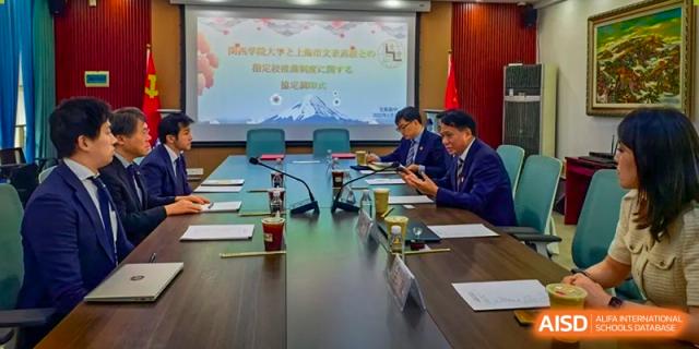 A group of students and possibly teachers sitting around a long table for a conference or meeting, with a presentation screen in the background at Shanghai Wenlai International School.