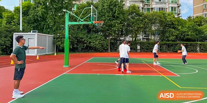 An empty outdoor basketball court with a green and red surface, with two people standing on it in the distance at Shanghai Wenlai International School.