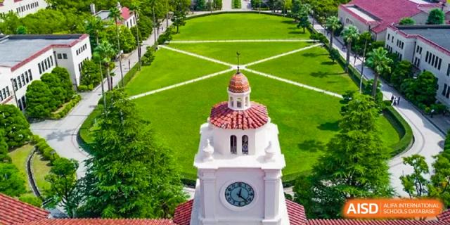 An elevated view of a clock tower with a red roof, set against a backdrop of a lush, manicured green lawn at Shanghai Wenlai International School.