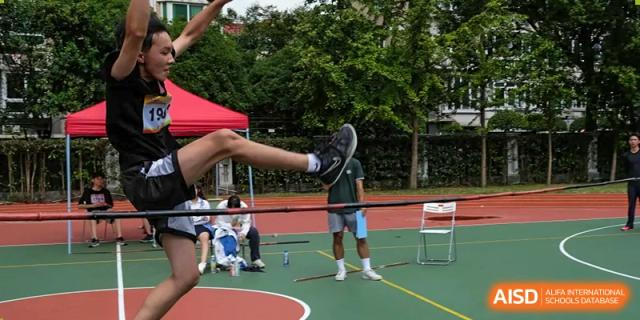 A student attempting a high jump over a bar on a track and field setup at Shanghai Wenlai International School.