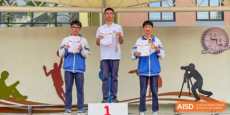 Three male students standing on a podium and holding up their certificates and medals after a competition at Shanghai Wenlai International School.