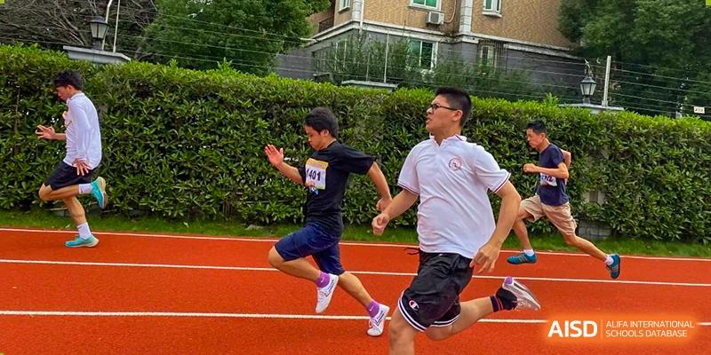 Male students from Shanghai Wenlai International School running hard during a sporting event on a red track.