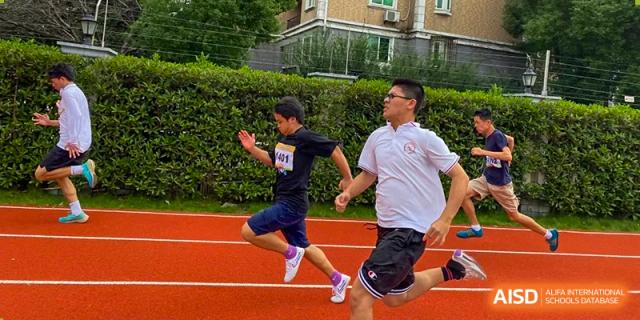 Male students from Shanghai Wenlai International School running hard during a sporting event on a red track.
