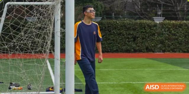 A student in a blue and yellow school sports uniform standing on a green field at Shanghai Wenlai International School.