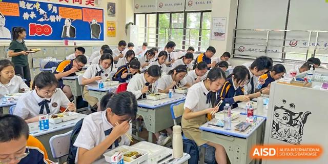 A wide view of a classroom full of students sitting at their desks and eating boxed lunches at Shanghai Wenlai International School.