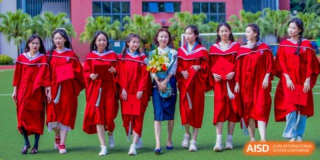 A group of female students and a teacher at Shenzhen (Nanshan) Concord College of Sino-Canada standing on a green field, some wearing graduation gowns.
