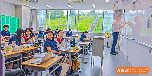 An aerial view of a classroom at Shenzhen (Nanshan) Concord College of Sino-Canada showing students and teachers with a scenic window view.