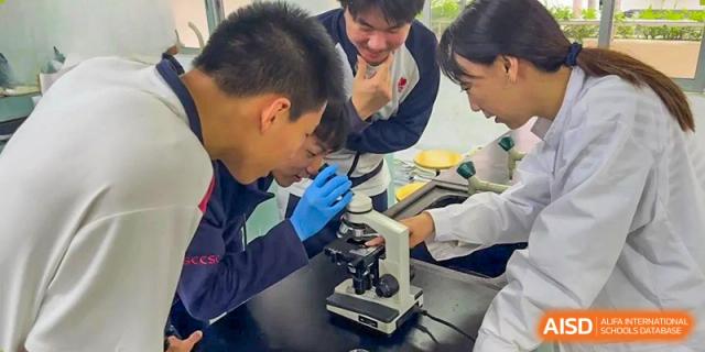 A teacher at Shenzhen (Nanshan) Concord College of Sino-Canada helping two students use a microscope in a science lab.