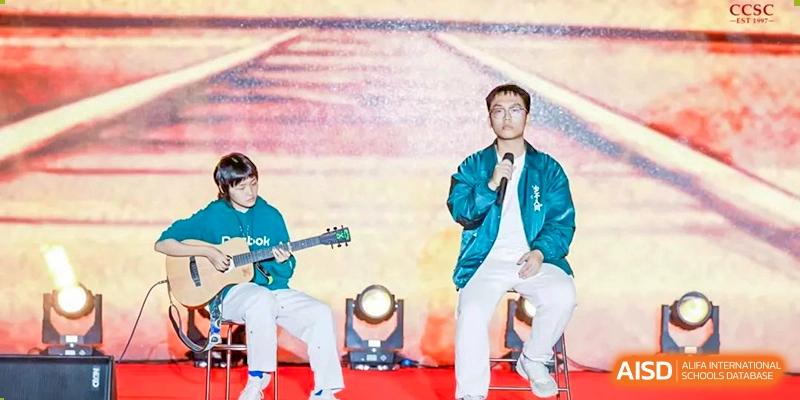 A male teacher at Shenzhen (Nanshan) Concord College of Sino-Canada singing on a stage during a school event.