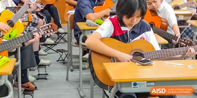 A close-up of a student at Shenzhen (Nanshan) Concord College of Sino-Canada playing an acoustic guitar in a classroom.