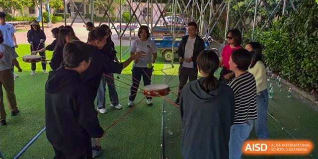 Students at Shenzhen (Nanshan) Concord College of Sino-Canada holding a large rope while playing a team game outdoors.