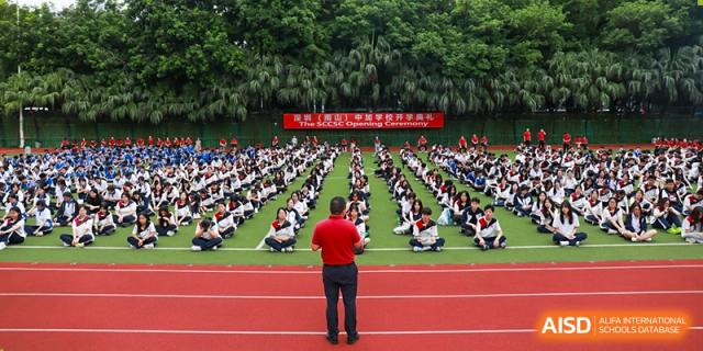 A large group of students at Shenzhen (Nanshan) Concord College of Sino-Canada seated in rows on the field, facing a leader.