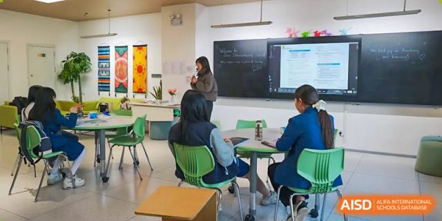 A teacher instructs students sitting at green chairs and desks in a modern classroom at Sias International School.
