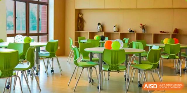 An empty classroom or common area at Sias International School with bright green chairs, round tables, and shelves containing toys and decorations.