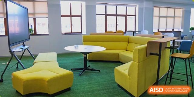 A modern student lounge area at Sias International School with bright yellow curved seating, a white table, and green carpet.