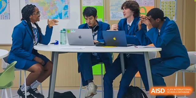 Two male students at Sias International School collaborate on a project, working together on laptops at a shared table.