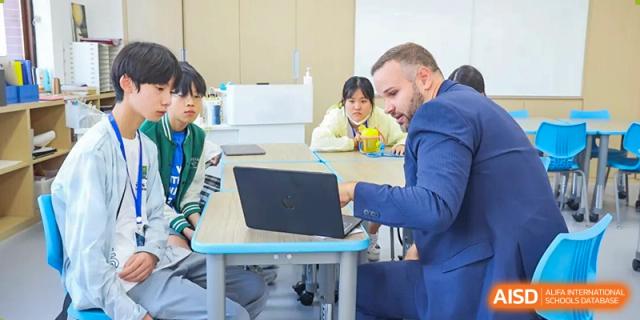 Students and a teacher work together on a laptop at a table in a bright classroom at Sias International School.