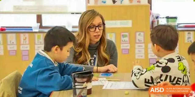 A teacher at Sias International School helps two young students with a hands-on activity at a desk.