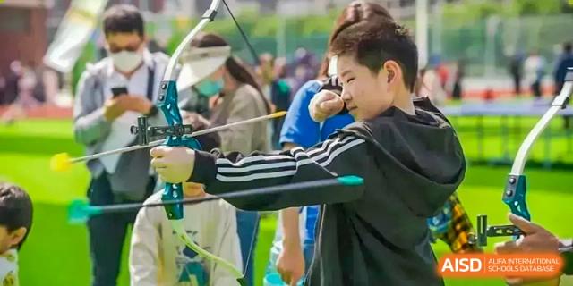 A Sias International School student in a sun visor practicing archery outdoors with a bow and arrow.