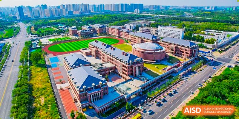 Sias International School campus aerial view showing large, traditional brick buildings, sports fields, and a surrounding city skyline.