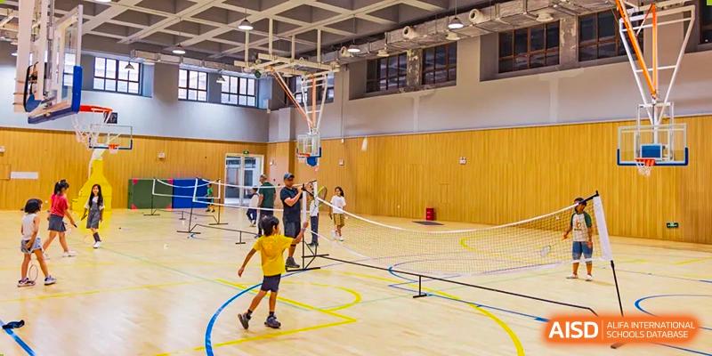 Students playing badminton and basketball on a wood court inside the Sias International School sports center.