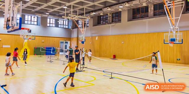 Students playing badminton and basketball on a wood court inside the Sias International School sports center.