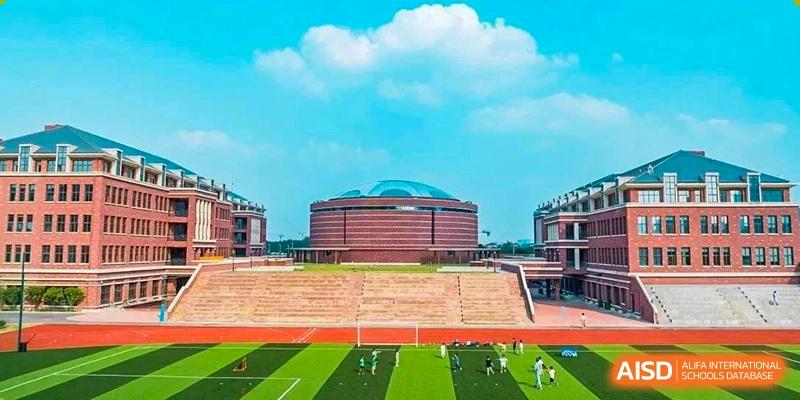 Outdoor view of the Sias International School stadium and large sports field under a bright, blue sky, with students playing on the grass.