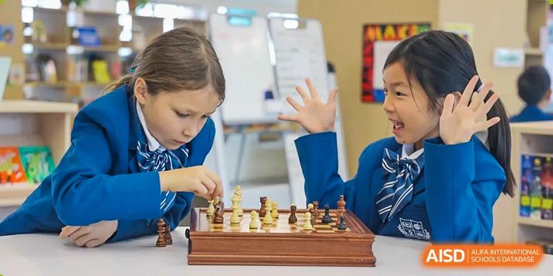 Young student at Sias International School intently playing a game of chess, reaching out to move a piece on a wooden chessboard.