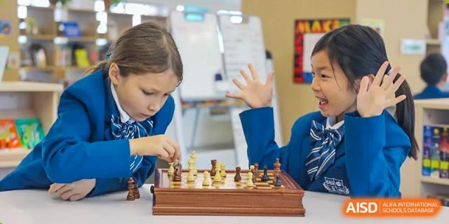 Young student at Sias International School intently playing a game of chess, reaching out to move a piece on a wooden chessboard.