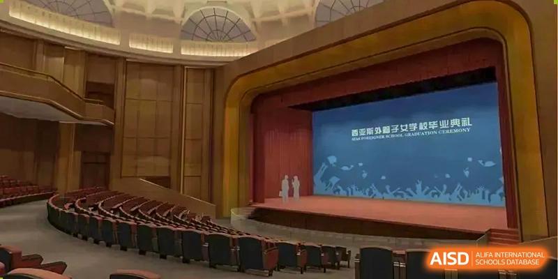 Interior view of the large auditorium stage at Sias International School with a screen backdrop, an arching ceiling, and tiered seating in the foreground.