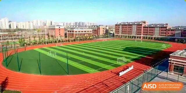 Aerial view of the large outdoor soccer and sports field at Sias International School with green turf, red track, and school buildings in the background.