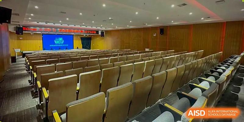 Rows of empty, cushioned seating in a spacious auditorium or lecture hall at Sias International School, with wood-paneled walls and an illuminated ceiling.