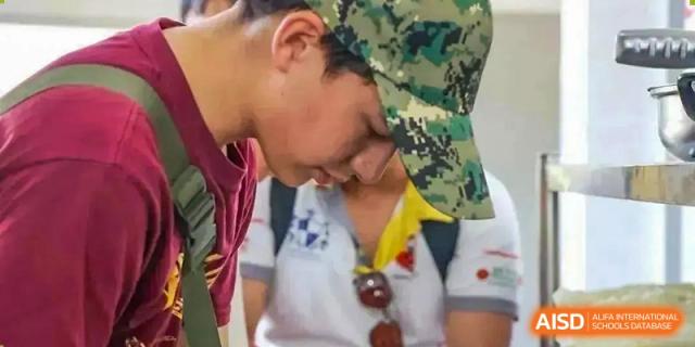 Close-up of an older student from Sias International School in a camouflage hat interacting gently with a younger student.